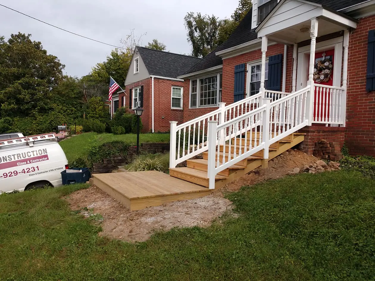New wood steps and landing with white vinyl railings leading to the red front door of a brick house
